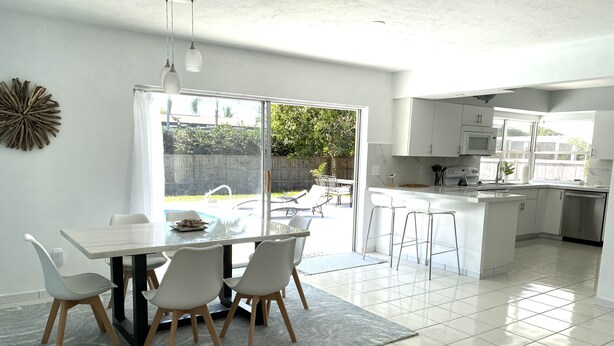 A modern kitchen with white cabinets, a stainless steel dishwasher, and a large window overlooking a backyard. - Great location! Marco Island home with pool that’s just 2miles to beaches (Marco Island)