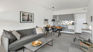 Una sala de estar moderna con un sofá gris, una mesa de centro y un comedor con una mesa y sillas de madera.