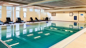 Una piscina con agua cristalina, rodeada de sillas de descanso y una solana empavedada.