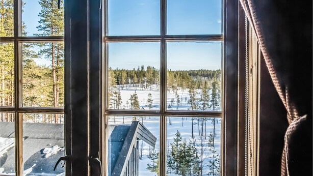 A view through a window with a clear sky, a snowy landscape, and a building with a sloped roof.