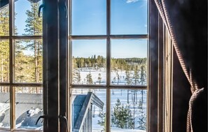 Blick durch ein Fenster auf eine verschneite Landschaft und ein Gebäude mit geneigtem Dach, bewölkter Himmel.