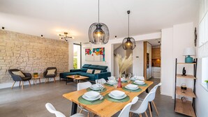 Uma sala de estar moderna com parede de pedra, sofá azul e área de jantar para seis pessoas, com cadeiras brancas e mesa de madeira.