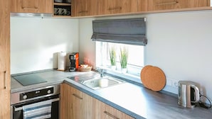 A modern kitchen with wooden cabinets, a built-in dishwasher, a stainless steel sink, and a kettle.