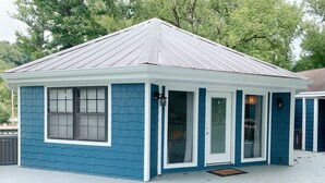 A small, single-story building with a blue exterior and white trim, featuring a front porch and a metal roof. - The Tree House! (Florence)