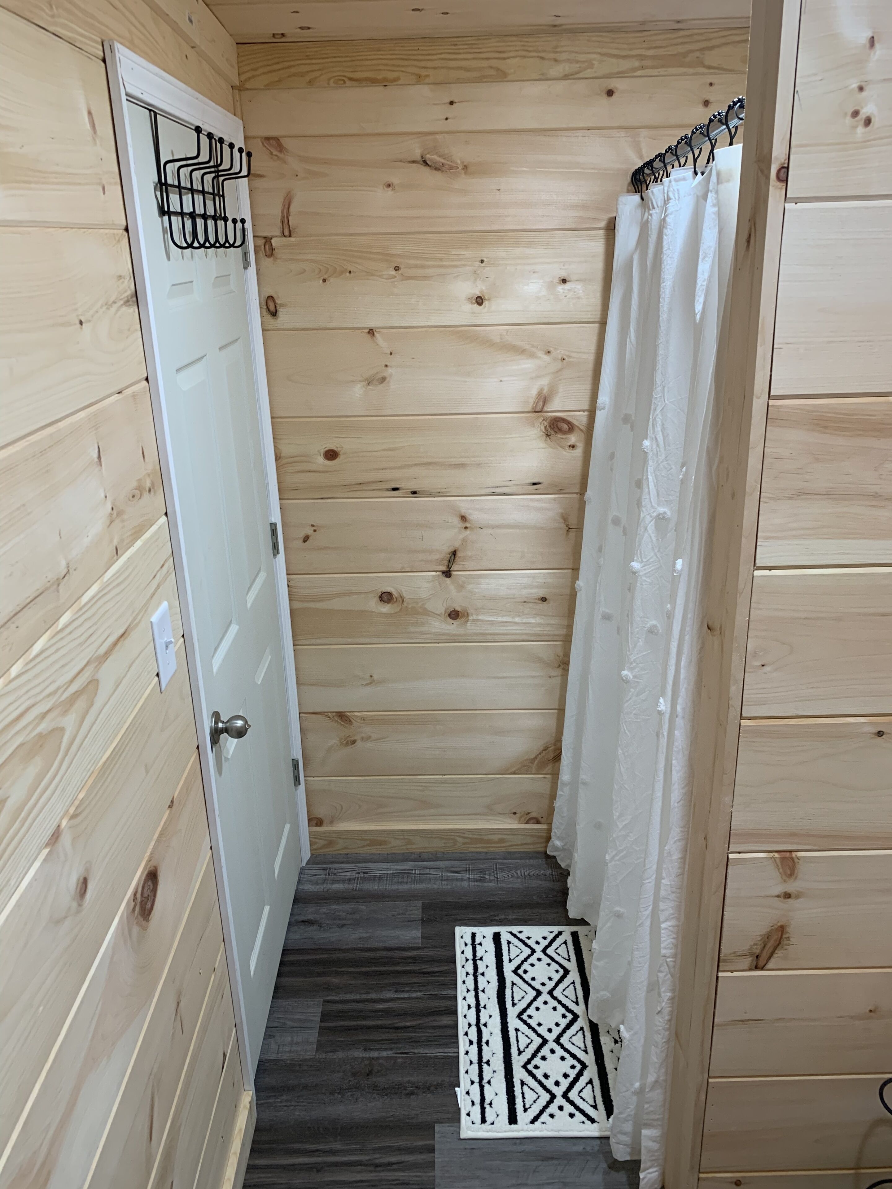 Corredor interno de madeira com uma porta branca, um cabide de metal e um tapete estampado.