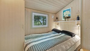 A bedroom with a bed, a window, a painting, and a shelf with decorative items.