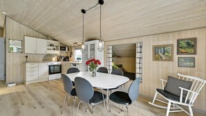 A modern kitchen with white cabinets, a microwave, and a stove. There is a dining area with a white table and black chairs.