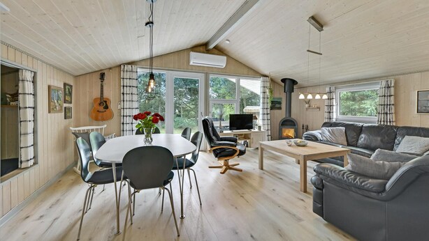 A spacious living room with a high ceiling, wooden floors, a fireplace, a sofa, a dining table with chairs, and a television.