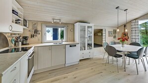 A modern kitchen with white cabinetry, a built-in dishwasher, and a dining area with a round table and chairs.