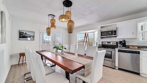 Una cocina moderna con armarios blancos, electrodomésticos de acero inoxidable y una mesa de comedor de madera con sillas blancas.
