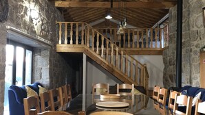 Uma sala de jantar com escada de madeira, paredes de pedra e teto alto.