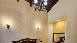 Een slaapkamer met een houten bed, nachtkastje, lamp, spiegel aan de muur en een kroonluchter.