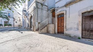 A cobblestone street with historic buildings, a staircase leading to a second floor, and a wooden door. - Pet friendly apartment in Carovigno (Carovigno)