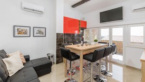 Una cocina moderna con armarios rojos, una zona de comedor con una mesa de madera y sillas negras, y un sofá de cuero negro con cojines.