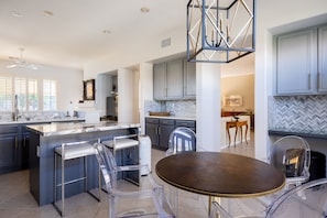 A modern kitchen with a central island, bar stools, and a dining table.