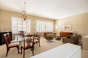 A spacious living room with a dining area, large windows, and a chandelier.