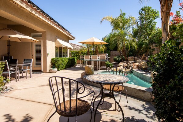 A patio with outdoor furniture, a swimming pool, and surrounding greenery.