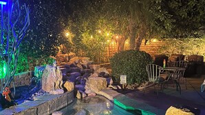 A nighttime outdoor pool area with rocks, a small waterfall, and seating. - Luxury, spacious, spa home, sleeps 8, Chef Kitchen, office, and separate casita. (Palm Desert)