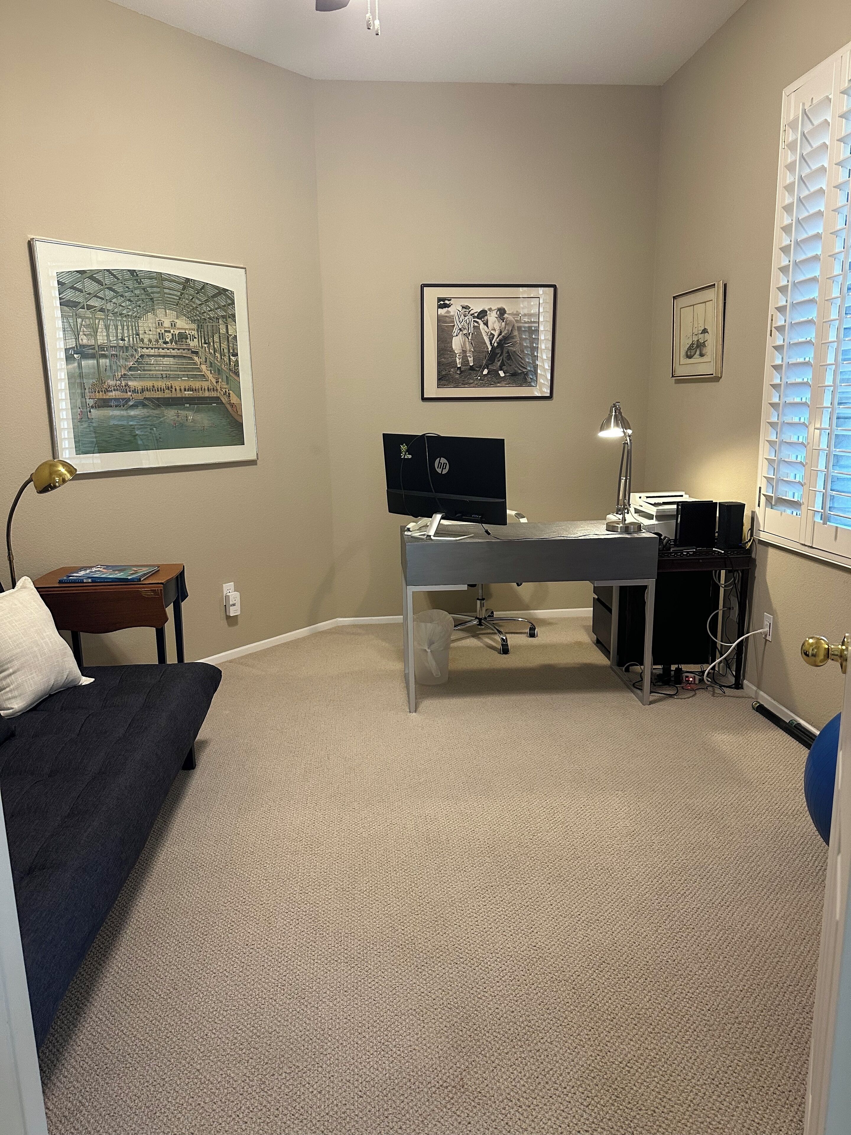 A room with a desk, computer, lamp, and a bed.
