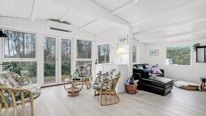 En rummelig stue med store vinduer, fletningsmøbler, en sort sofa og en hvid lampe.