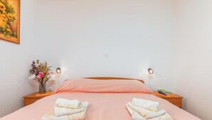 A neatly made bed with pink bedding, two folded towels, a vase with flowers, and two wall-mounted lamps. - Beautiful apartment in Fazana with WiFi (Fazana)