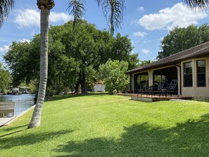 Une pelouse bien entretenue, un patio couvert avec des meubles d’extérieur, et une étendue d’eau avec un quai et un petit bâtiment à proximité.