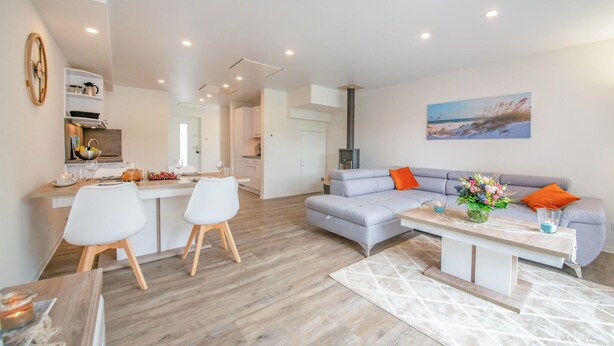 Un salon moderne avec un canapé gris, une table basse et un coin repas comprenant des chaises blanches et une table en bois.