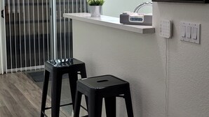 Eine moderne Küche mit weißer Arbeitsplatte, zwei schwarzen Barhocker, einer Pendelleuchte und einem gerahmten Tierbild an der Wand.