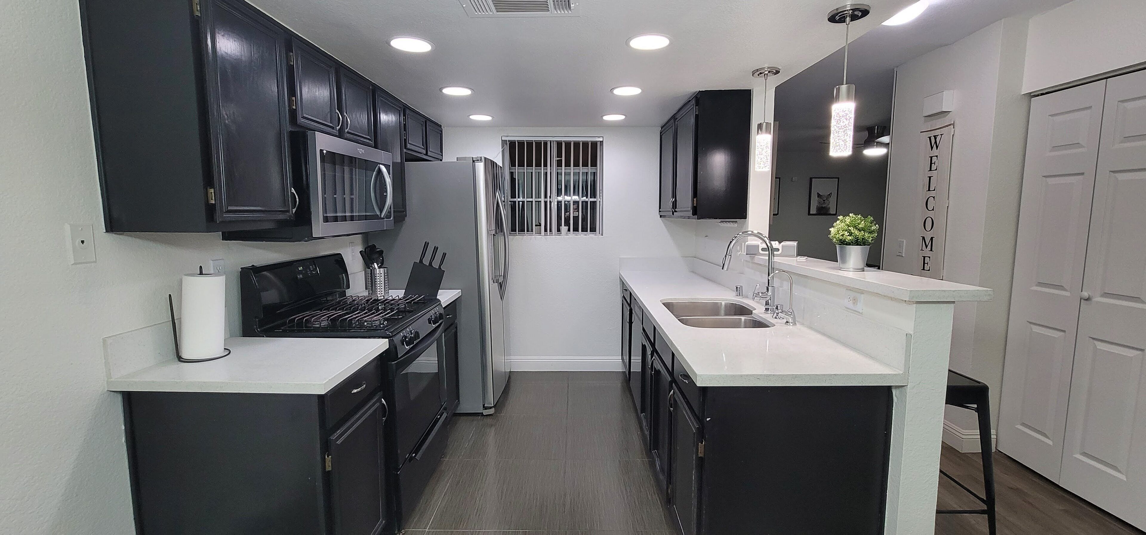 A modern kitchen with black cabinets, a white countertop, a stainless steel sink, and a built-in oven.