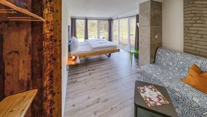 Een moderne slaapkamer met een hoogslaper, grote ramen, een groene fauteuil en een gestreept sofa.