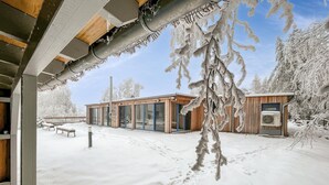 Een houten gebouw met grote glazen deuren en ramen, omgeven door met sneeuw bedekte bomen.
