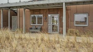 En moderne bygning med en udhængende betonkonstruktion, en glasdørindgang og et siddeområde med stol og bord.