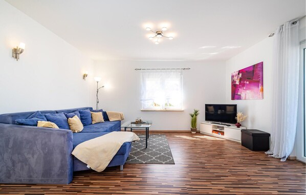 A modern living room with a blue sofa, a small table, a TV, and a large window with curtains.