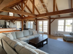 A spacious living room with a large sectional sofa, a coffee table, and a dining area with a table and chairs. The room features exposed wooden beams and large windows allowing natural light. - 4 Bedroom, Upside Down Post and Beam Nantucket Home (Nantucket)