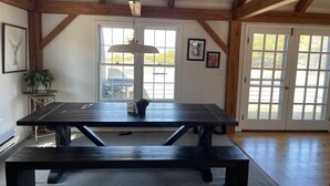 A spacious room with a large dark wooden table and benches, a ceiling fan, and large windows with a view of the outdoors. - 4 Bedroom, Upside Down Post and Beam Nantucket Home (Nantucket)