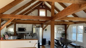 A spacious loft with a high ceiling, exposed wooden beams, a kitchen with modern appliances, a dining area with a large table, and a cozy seating area. - 4 Bedroom, Upside Down Post and Beam Nantucket Home (Nantucket)