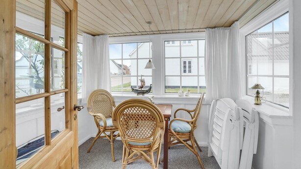 A room with a wooden ceiling, large windows, wicker chairs, a table, and a radiator. - Lovely home in Thisted with kitchen (Thisted)