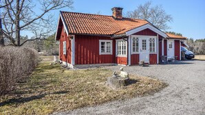 Ein rotes Holzhaus mit einem Ziegeldach und einer Veranda, davor ist ein Auto geparkt.