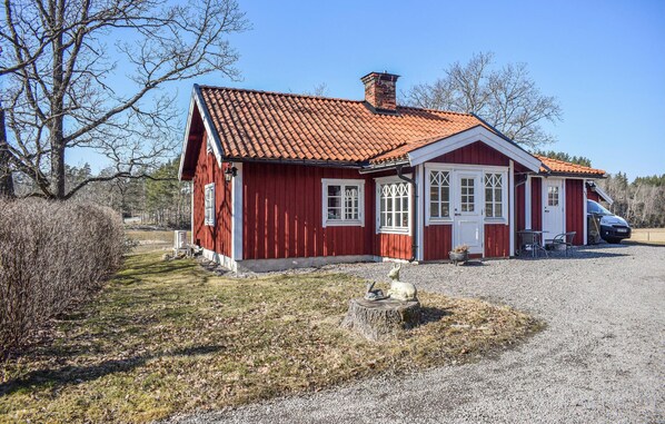 Une maison en bois rouge, avec un toit en tuiles, un porche à l’avant et une voiture garée devant.