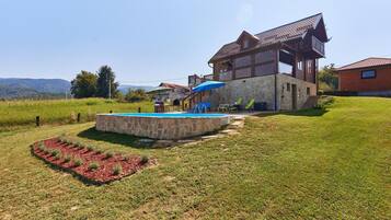 A stone pool with a wooden deck, surrounded by a well-maintained lawn and a decorative garden bed.