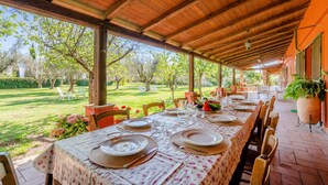 An outdoor covered dining area with tables set for a meal, surrounded by a garden and trees. - Gorgeous home in Montalto di Castro (Montalto di Castro)