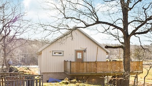 A single-story wooden house with a small porch, surrounded by trees and a grassy yard.