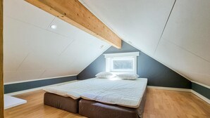 A small, sloped-roof bedroom with a bed, a window, and wooden beams.