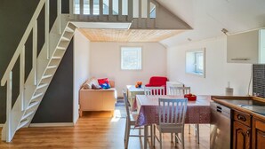 A spacious living area with a wooden staircase, a dining table with chairs, a red chair, and a kitchen area with a sink and cabinets.