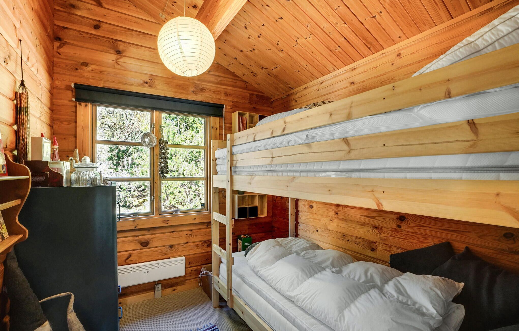 A cozy cabin room with a bunk bed, a desk, and a window with a view of trees.