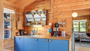 L’intérieur d’un chalet en bois comprend une cuisine avec des meubles bleus, une machine à café et un porte-couteaux suspendu.