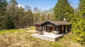 Une cabane dotée d’une véranda, de meubles de jardin et offrant une vue sur la forêt environnante.