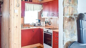 A compact kitchen with red cabinets, a stove, and a stone wall. - 2 bedroom beautiful home in Gol (Gol)