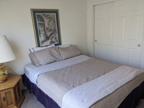 A bedroom with a bed, a nightstand, a lamp, and a framed picture on the wall.