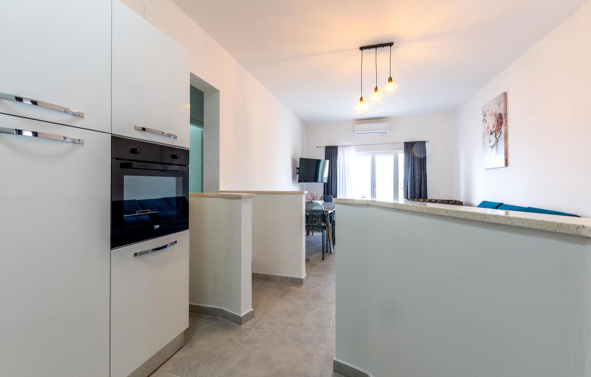 A modern kitchen with built-in appliances, a dining area with a table and chairs, and a living space with a sofa and a TV.